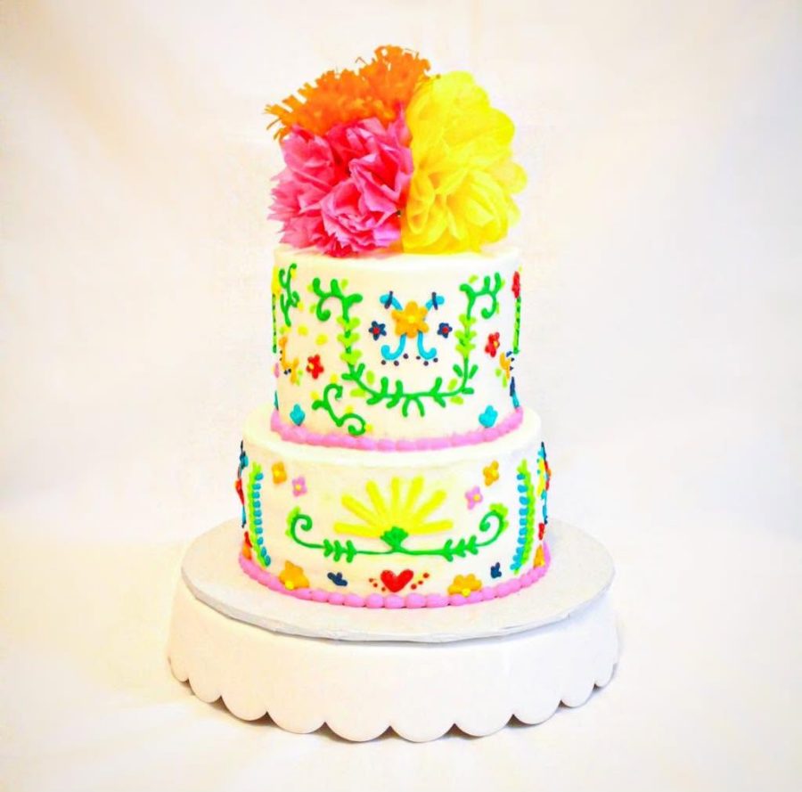Cakes & Bakes's own photograph: a two tier cake piped all over in bright Mexican embroidery patterns with paper flowers on top.