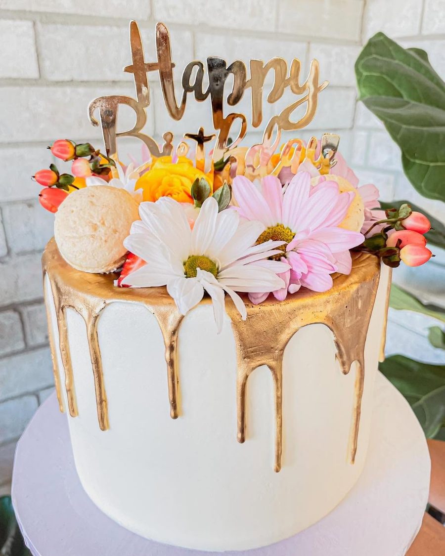 Cakes & Bakes's own photograph: a white buttercream cake with a gold drip and fresh flowers on top.