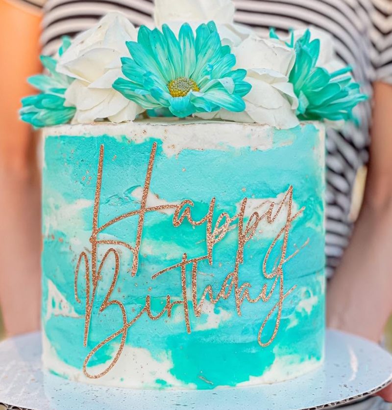 Cakes & Bakes's own photograph: a teal watercolour buttercream cake with gold lettering and fresh flowers.